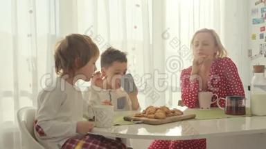 两个男孩在现代厨房吃早餐。 男孩吃带牛奶的饼干。 厨房里的白色桌子。 母亲和两个儿子